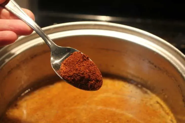 image of putting chili powder in a stock pot of chicken enchilada sauce