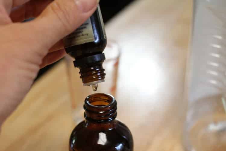 image of person putting essential oil drops in a brown glass bottle to make disinfectant spay