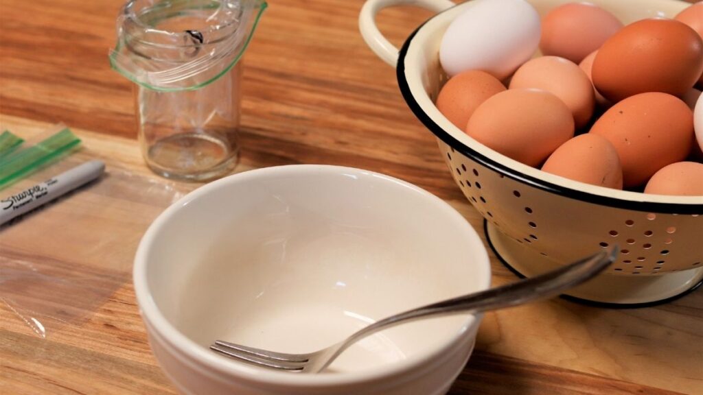 colander with farm fresh eggs on a wooden table with a white bow and fork, along with small ziplock bags and a half pint mason jar